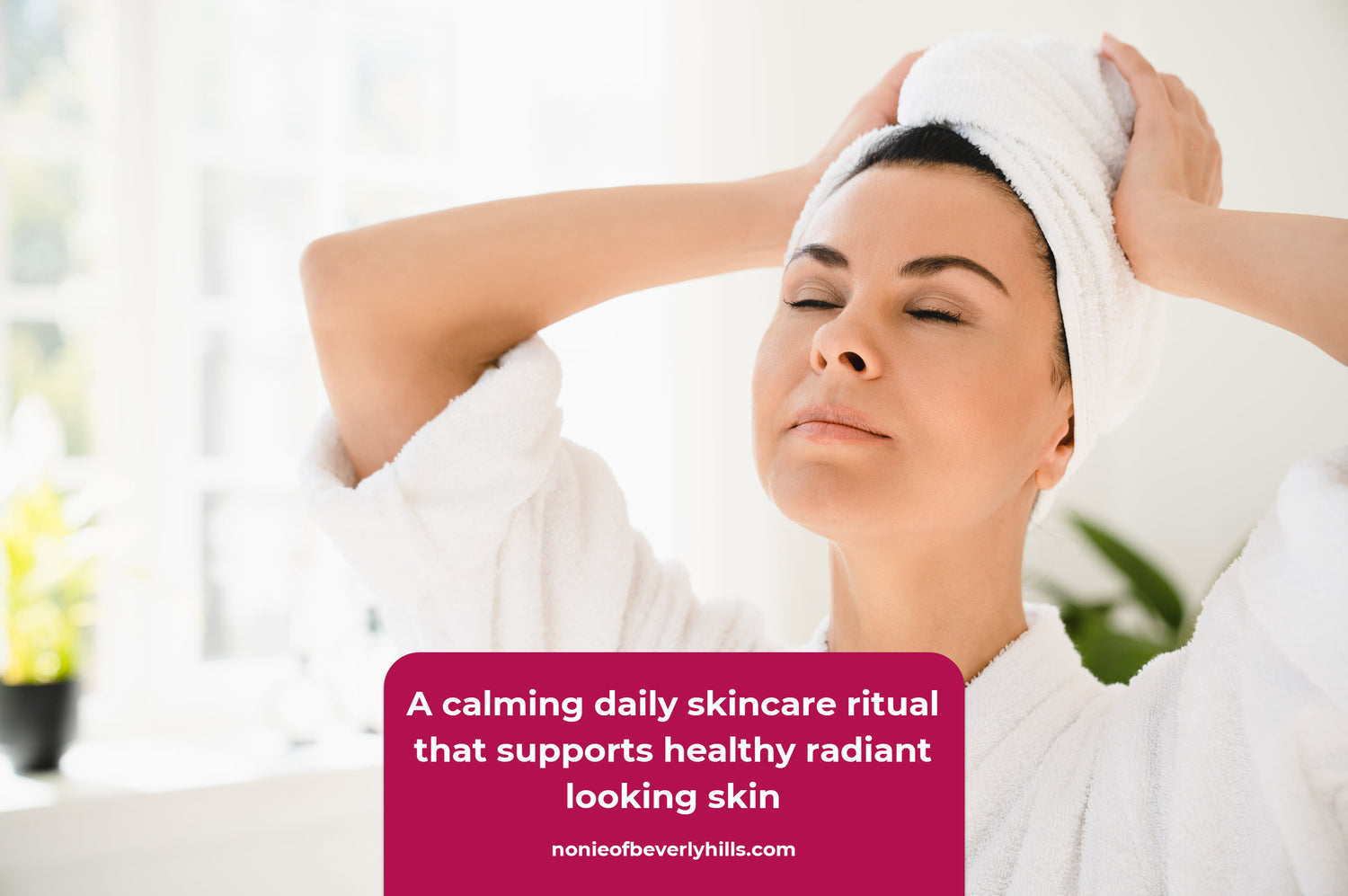 Woman in a white bathrobe with a towel wrapped around her hair standing in soft natural light with smooth radiant skin and a relaxed expression. A calm skincare ritual nurtures softer brighter looking skin and reflects the gentle results of plant powered AHA care.